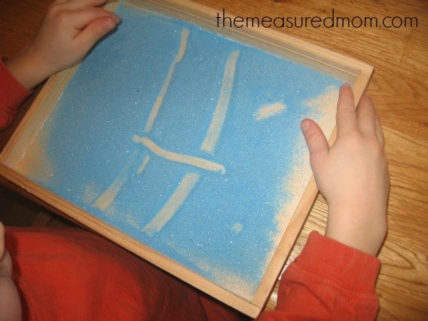 child making the letter H with colored sand