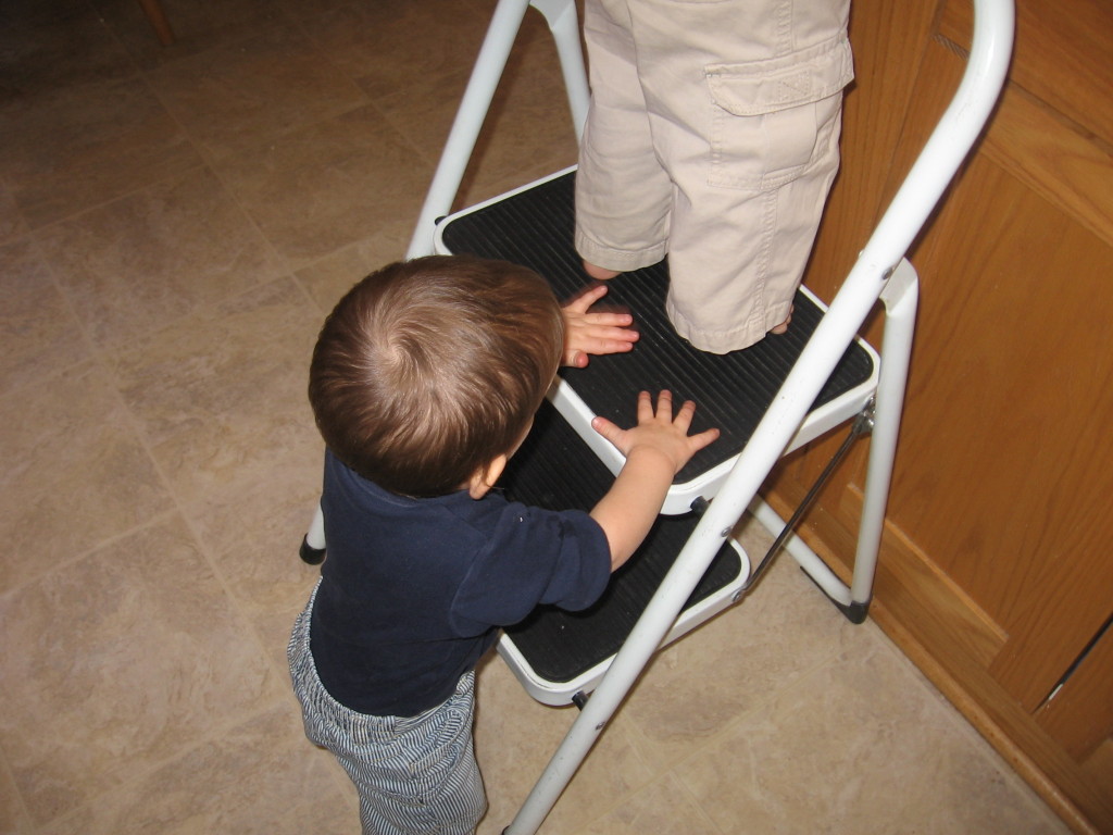 baby holding on to stool while child works