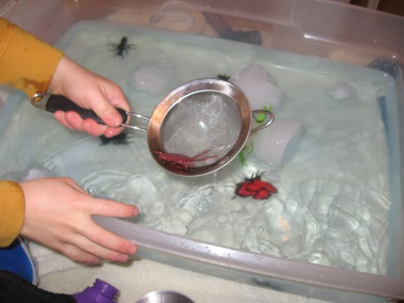 child fishing out toy cockroach with sieve