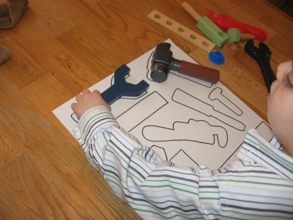 child placing toy tools on paper