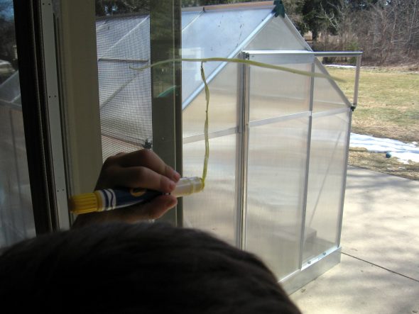 child writing on window making letter T with Crayola window crayons
