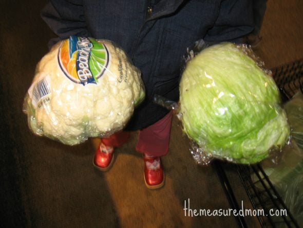 child holding up cauliflower and lettuce