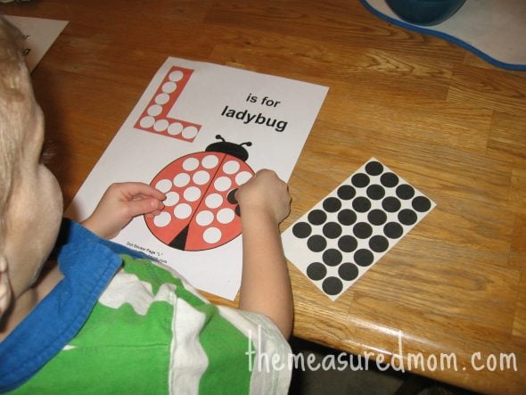 child placing dot sticker on letter L worksheet