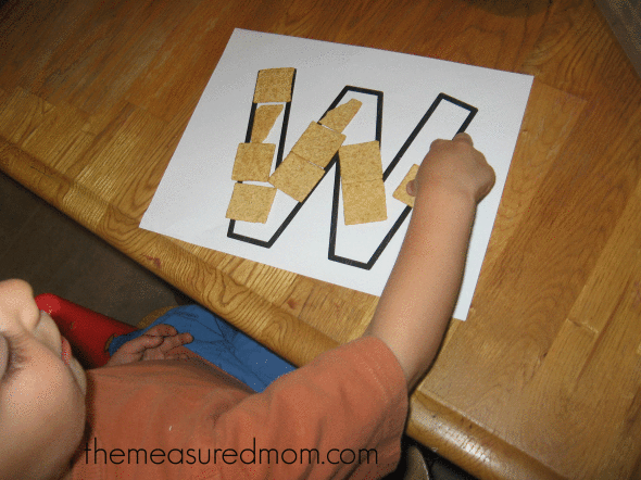 child filling letter W outline with Wheat Thins