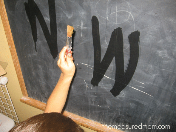 child writing letter W with water on chalkboard