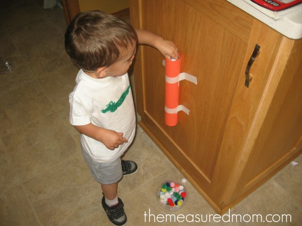 child poking pom-poms through a paper towel tube