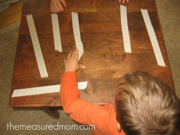 child placing masking tape on table